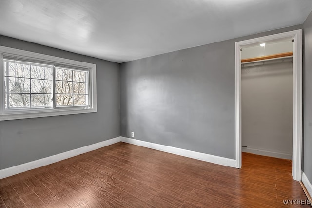 unfurnished bedroom featuring a spacious closet, wood finished floors, baseboards, and a closet