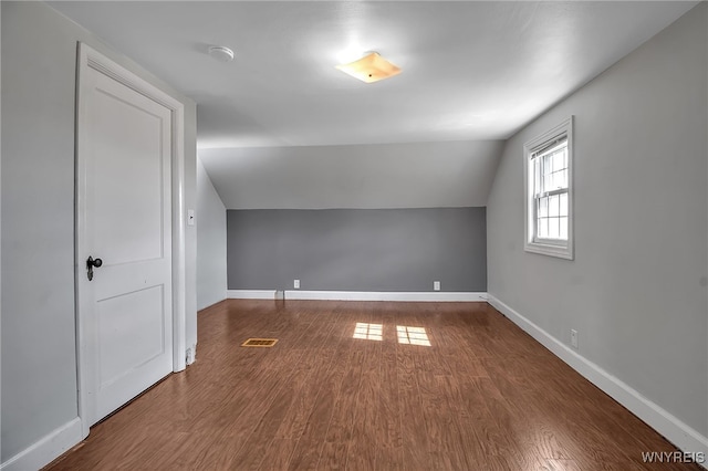 additional living space with vaulted ceiling, wood finished floors, baseboards, and visible vents