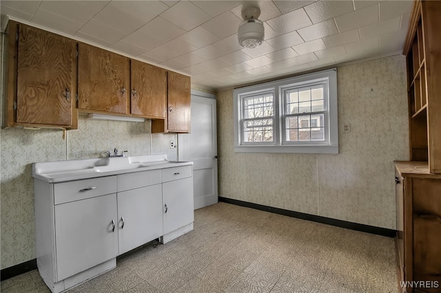 kitchen with wallpapered walls, light countertops, baseboards, and a sink