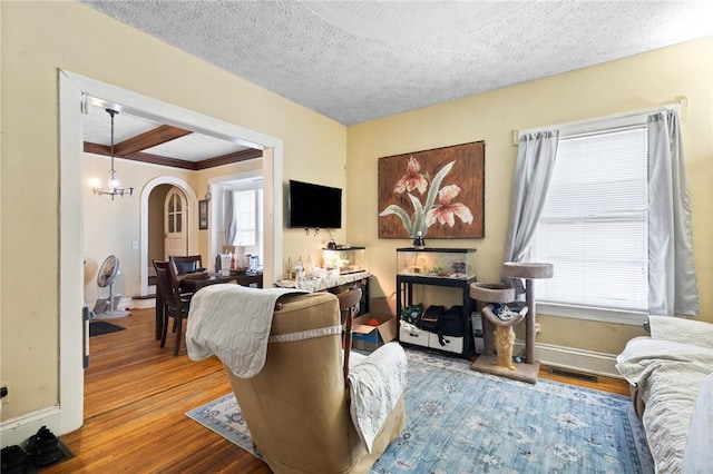 living area featuring a textured ceiling, wood finished floors, arched walkways, baseboards, and a chandelier