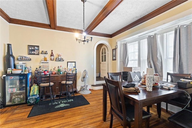 dining area featuring beam ceiling, wood finished floors, arched walkways, baseboards, and a dry bar