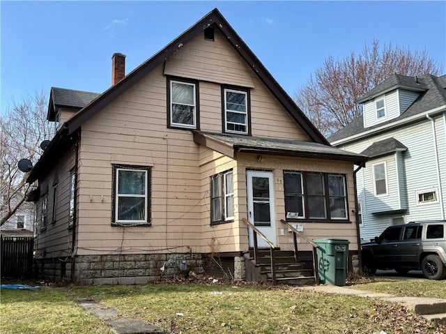 bungalow-style home featuring a front lawn, roof with shingles, a chimney, and entry steps
