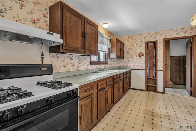 kitchen with under cabinet range hood, a sink, range with gas cooktop, wallpapered walls, and light floors