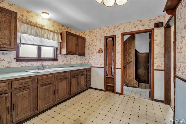 kitchen with light floors, wallpapered walls, and a sink