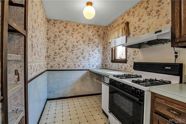 kitchen featuring wallpapered walls, gas range oven, light floors, and under cabinet range hood