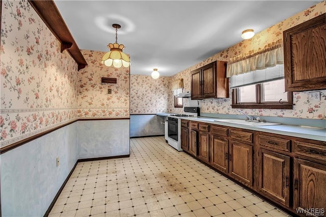 kitchen with light floors, wallpapered walls, white range with gas stovetop, a sink, and wainscoting