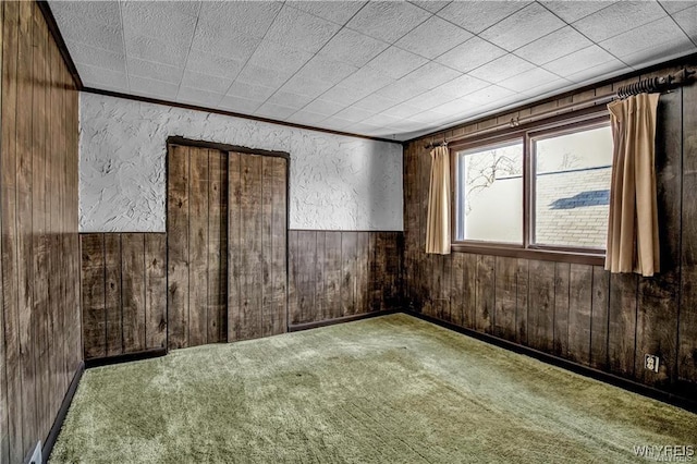 spare room featuring a textured wall, carpet, wood walls, and wainscoting