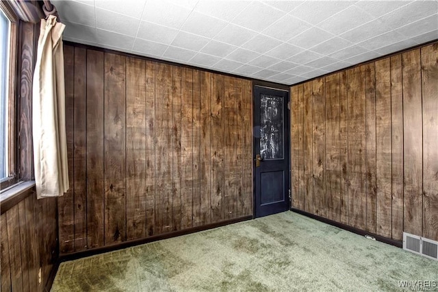 unfurnished room with wooden walls, visible vents, and carpet floors