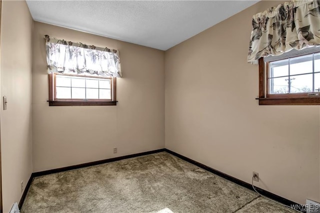 unfurnished room with a wealth of natural light, baseboards, a textured ceiling, and carpet flooring