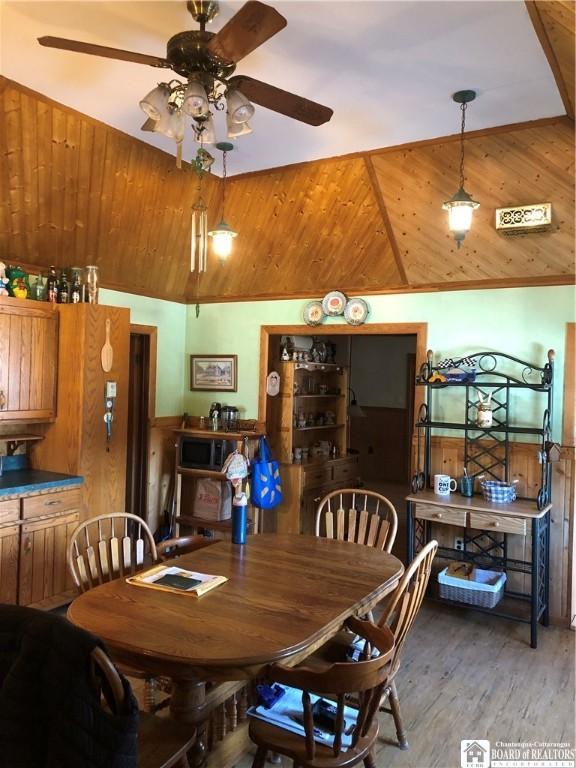 dining area with a ceiling fan, wood finished floors, vaulted ceiling, wood ceiling, and wood walls