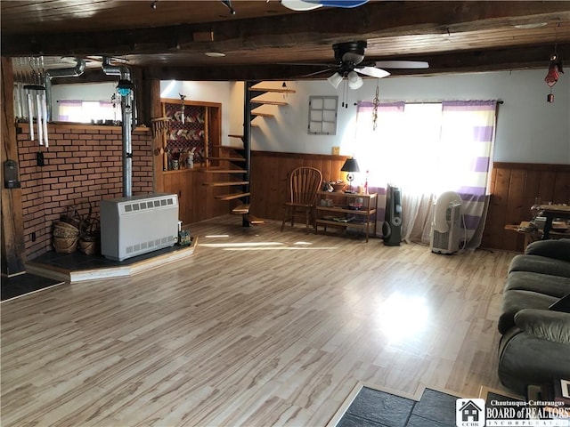 living area with wood finished floors, a wainscoted wall, beam ceiling, a wood stove, and stairs