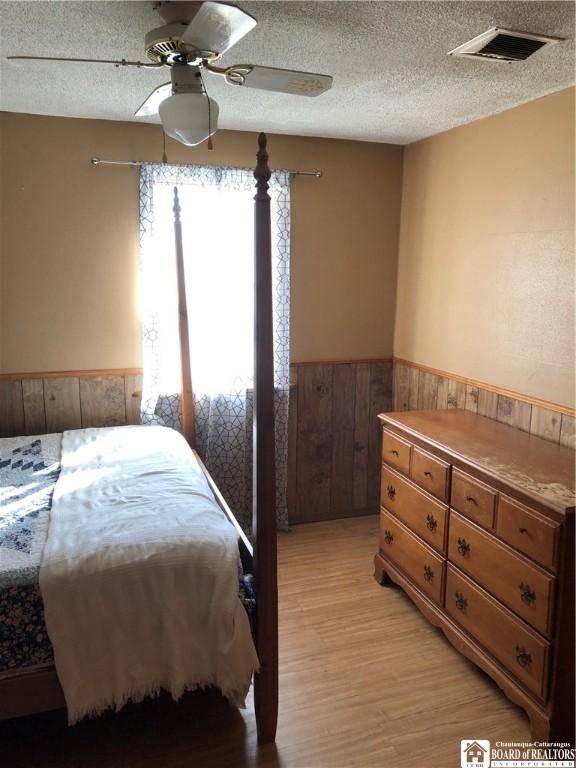 bedroom featuring a ceiling fan, visible vents, wainscoting, a textured ceiling, and light wood-type flooring