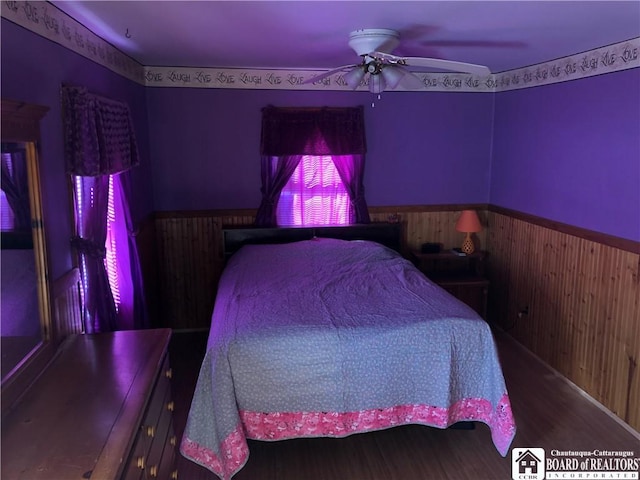 bedroom featuring a wainscoted wall, ceiling fan, wooden walls, and wood finished floors