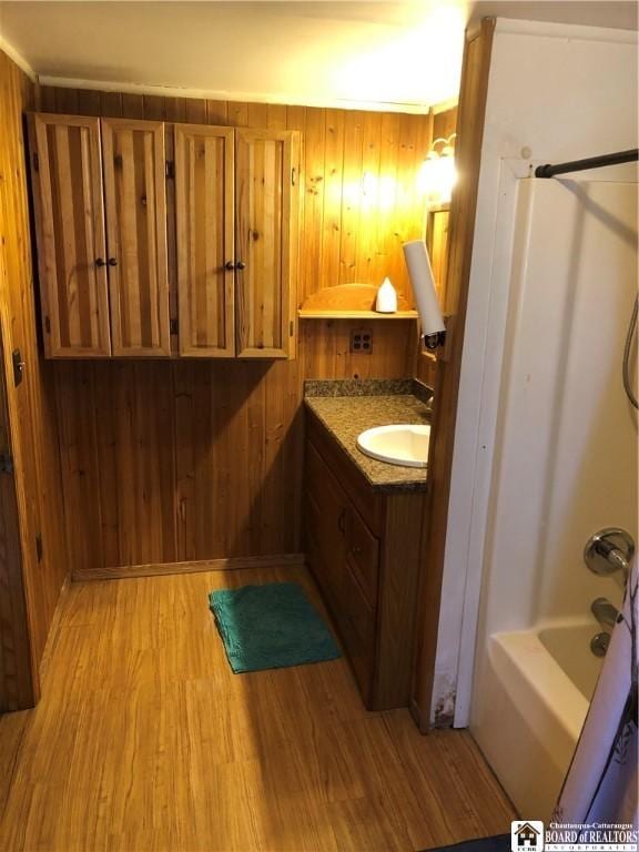 bathroom with vanity, shower / bathing tub combination, wooden walls, and wood finished floors