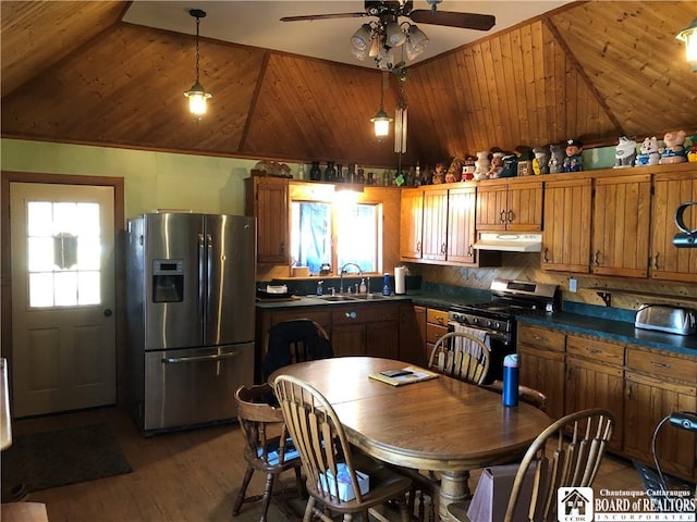 kitchen with dark countertops, under cabinet range hood, brown cabinets, stainless steel appliances, and a sink