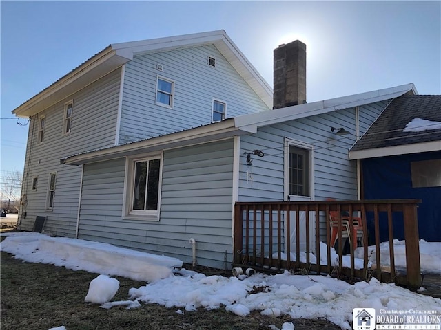 snow covered rear of property featuring a chimney