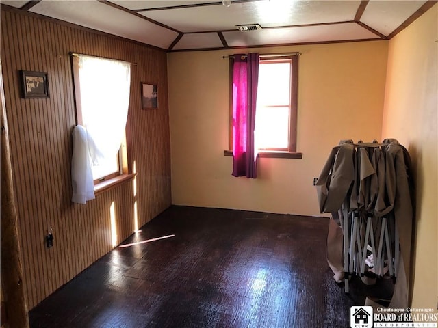 empty room featuring a wealth of natural light, visible vents, wood finished floors, and vaulted ceiling