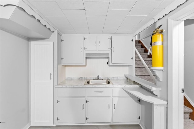 kitchen with white cabinetry, light countertops, baseboards, and a sink