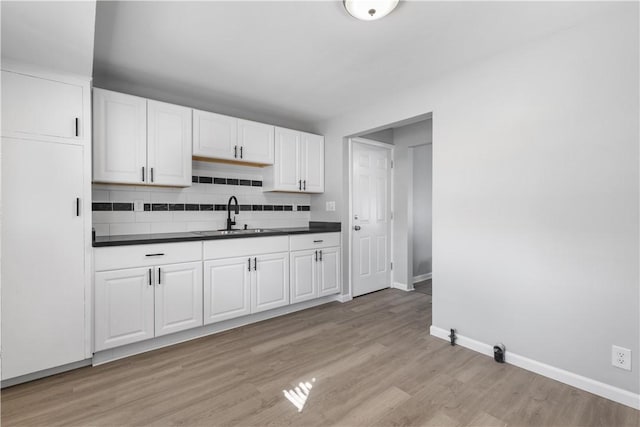 kitchen featuring baseboards, light wood-style flooring, a sink, dark countertops, and backsplash