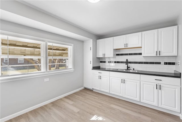 kitchen featuring dark countertops, backsplash, baseboards, light wood-style floors, and a sink