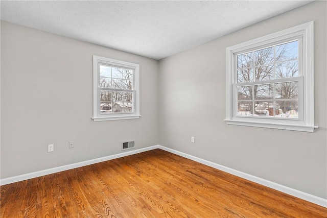 empty room with visible vents, baseboards, a textured ceiling, and wood finished floors