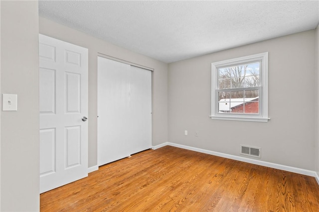 unfurnished bedroom with visible vents, light wood-style flooring, a textured ceiling, and baseboards