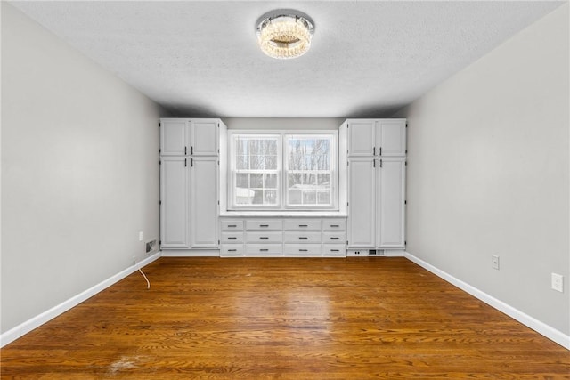 interior space with baseboards, a textured ceiling, and wood finished floors