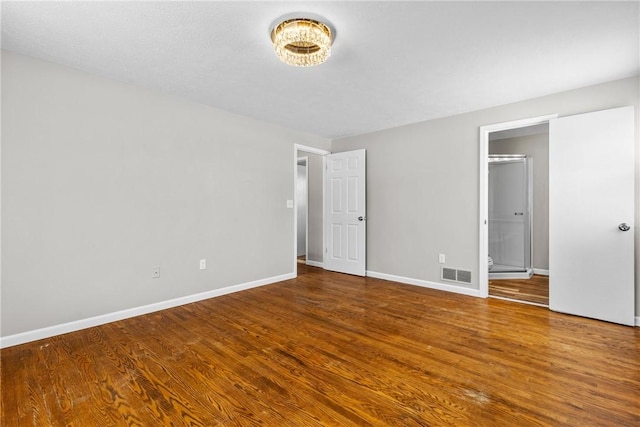 unfurnished bedroom with visible vents, baseboards, wood finished floors, and ensuite bathroom