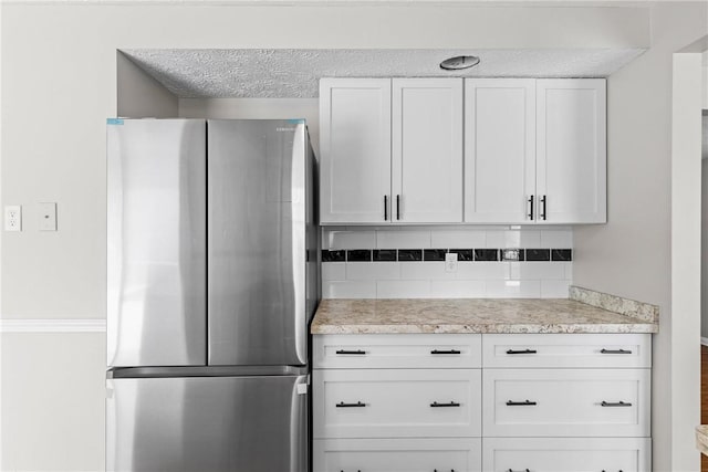 kitchen featuring freestanding refrigerator, decorative backsplash, light countertops, a textured ceiling, and white cabinetry