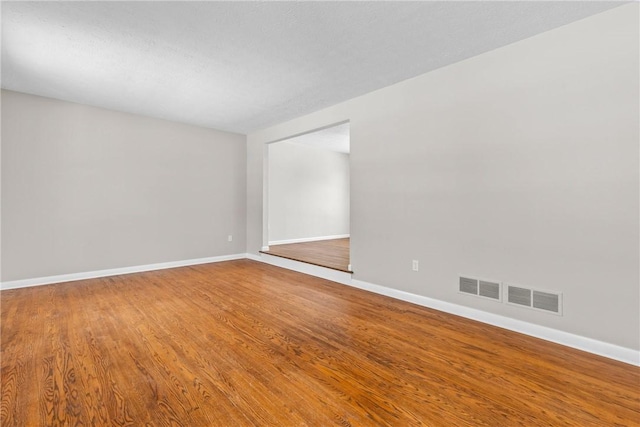 spare room with visible vents, baseboards, and wood finished floors