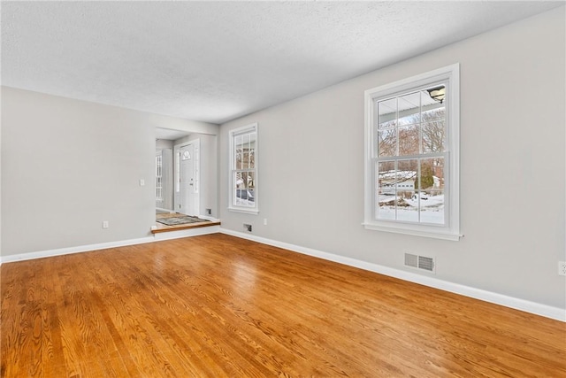 empty room with wood finished floors, visible vents, and baseboards