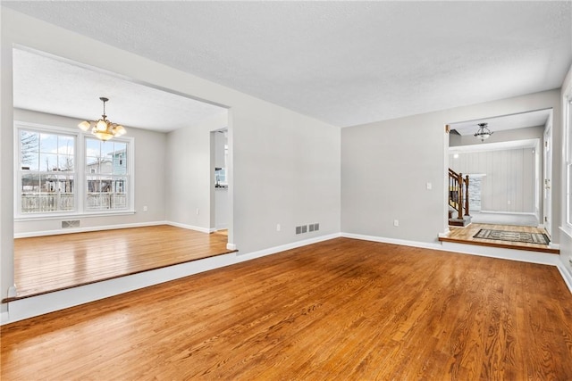 unfurnished living room with stairway, wood finished floors, visible vents, baseboards, and an inviting chandelier