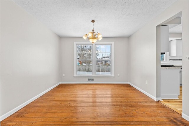 unfurnished dining area featuring baseboards, light wood-style floors, a chandelier, and a textured ceiling