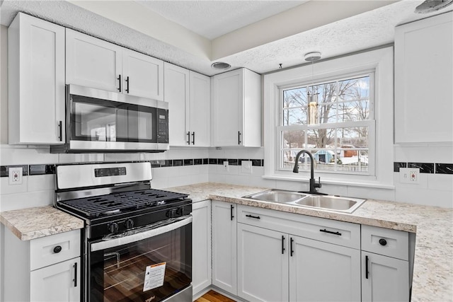 kitchen featuring a sink, stainless steel appliances, decorative backsplash, and white cabinetry