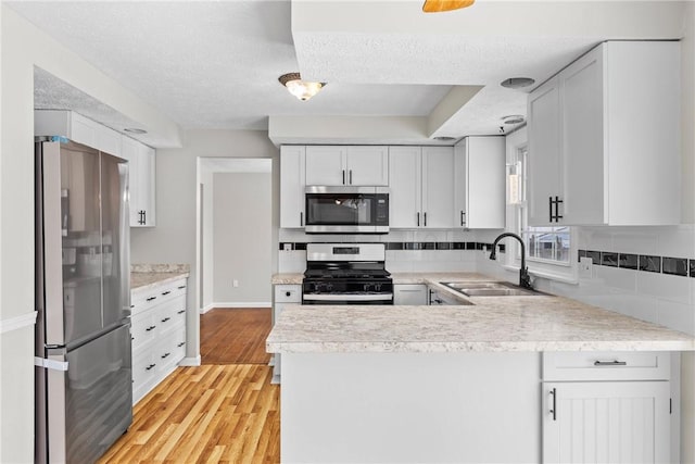 kitchen featuring a peninsula, light wood-style flooring, a sink, light countertops, and appliances with stainless steel finishes