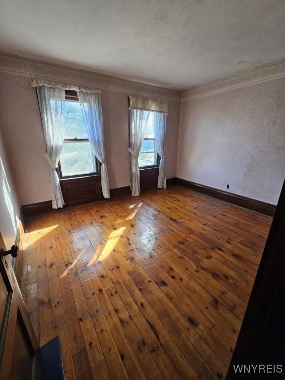 empty room featuring hardwood / wood-style flooring, crown molding, and baseboards