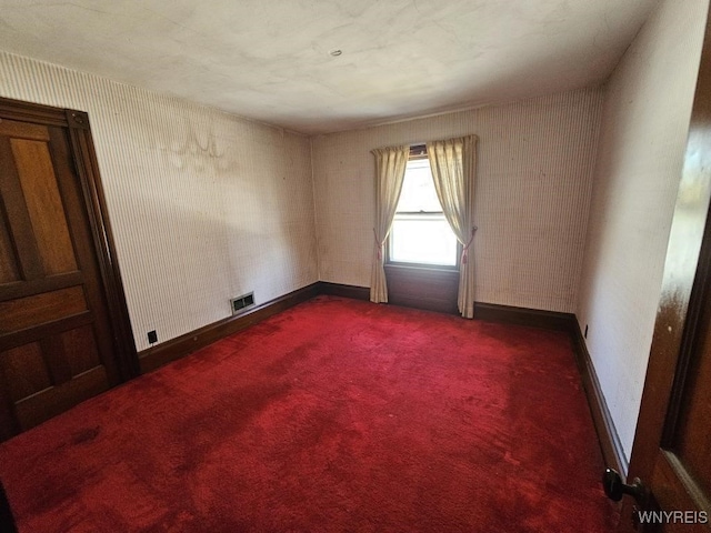 empty room featuring dark colored carpet, visible vents, baseboards, and wallpapered walls