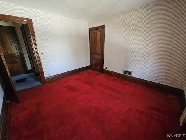 empty room with wallpapered walls, baseboards, visible vents, and dark carpet