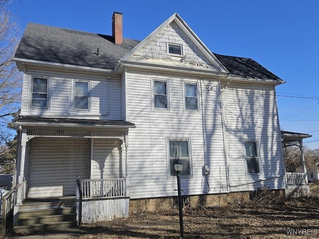 view of front of property featuring a porch, a chimney, and a shingled roof