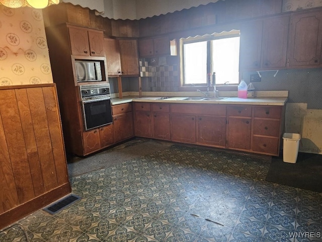 kitchen featuring oven, visible vents, wallpapered walls, wainscoting, and light countertops