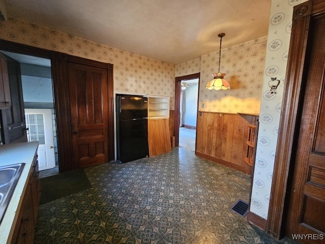 kitchen featuring a wainscoted wall, wallpapered walls, freestanding refrigerator, a sink, and dark floors