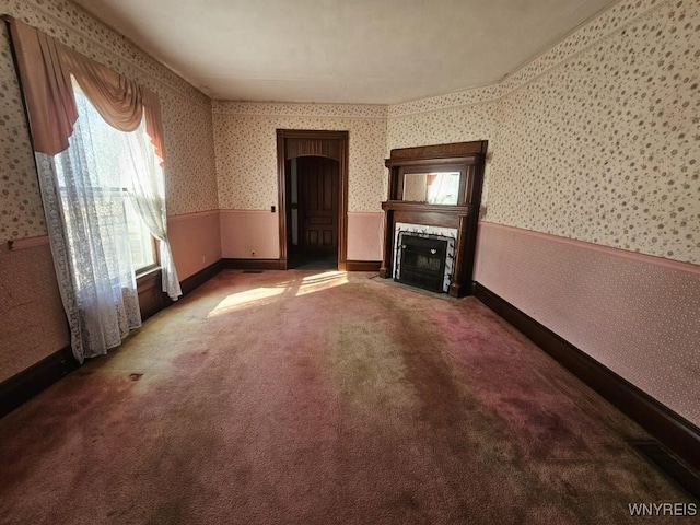 unfurnished living room featuring wallpapered walls, a fireplace with flush hearth, carpet flooring, and wainscoting