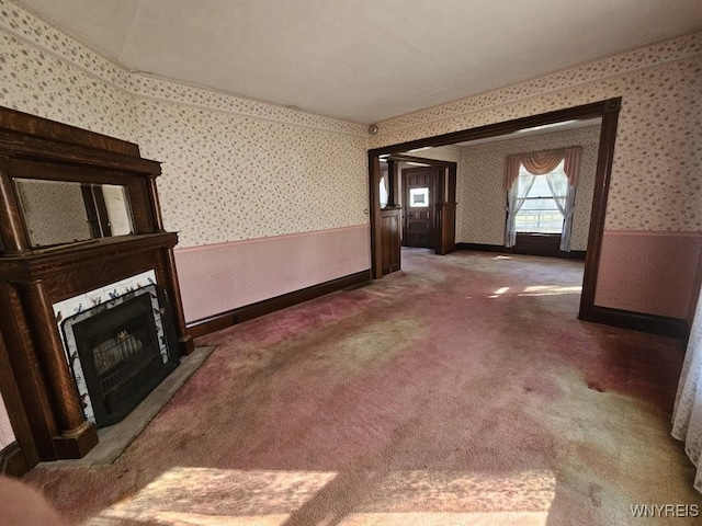 unfurnished living room featuring a wainscoted wall, a fireplace, wallpapered walls, and carpet