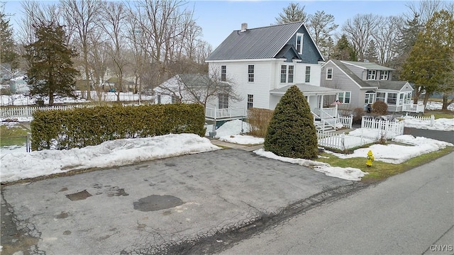 view of snowy exterior with metal roof, aphalt driveway, a chimney, and fence