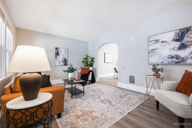 living area featuring wood finished floors, visible vents, baseboards, arched walkways, and a textured ceiling