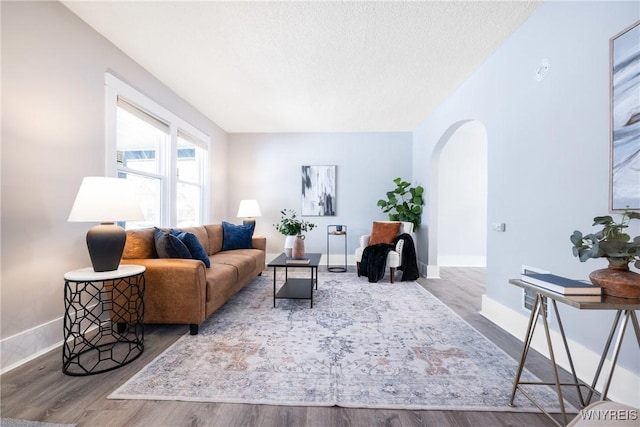 living room with baseboards, arched walkways, a textured ceiling, and wood finished floors