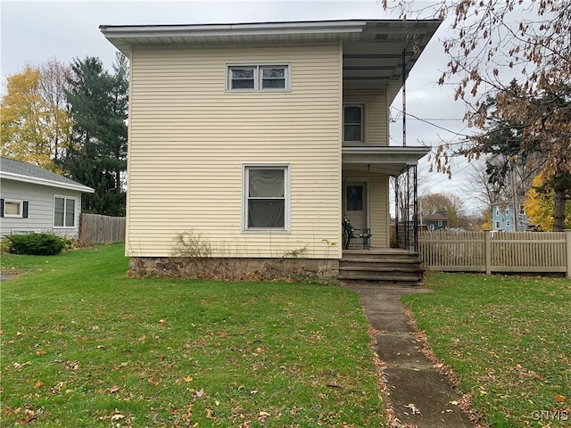 rear view of house featuring a lawn and fence