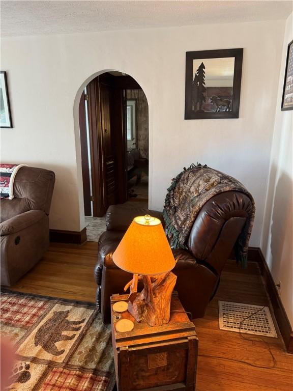 living area with baseboards, arched walkways, a textured ceiling, and wood finished floors