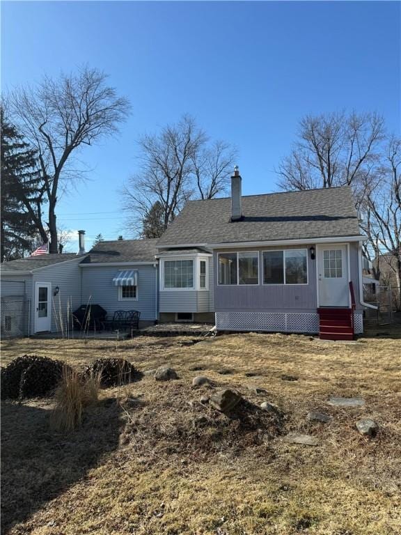 rear view of house featuring entry steps, roof with shingles, and a chimney