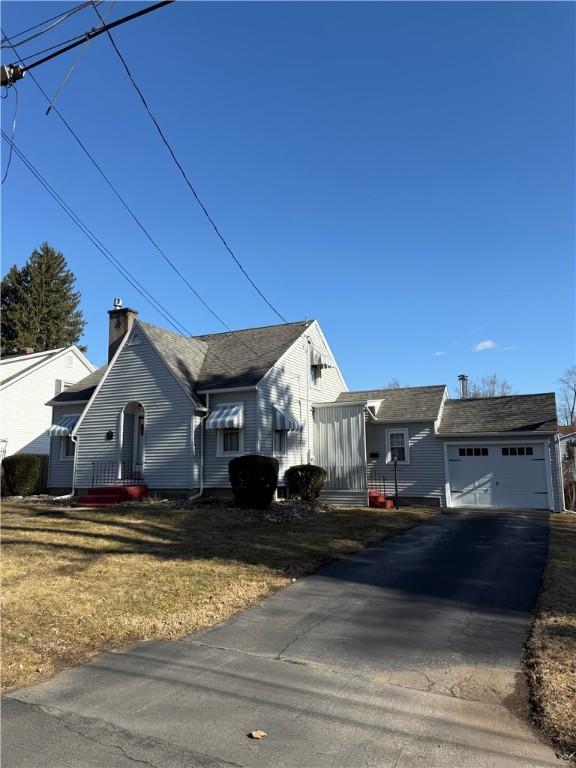 view of front of home featuring aphalt driveway, a front yard, a chimney, an outdoor structure, and an attached garage